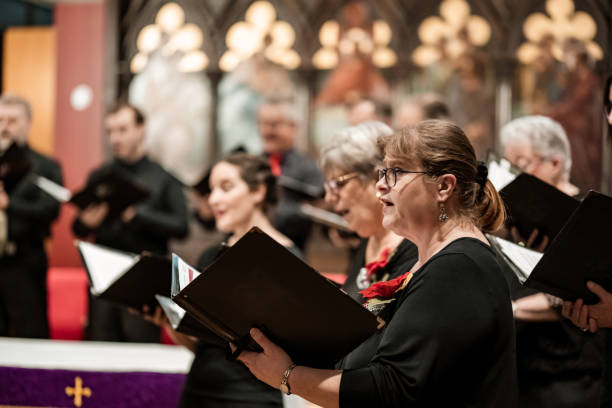 Church Choir during performance at Concert during Christmas Holiday season. Mixed age group of people dressed in all black attire. Interior of Anglican church at night.